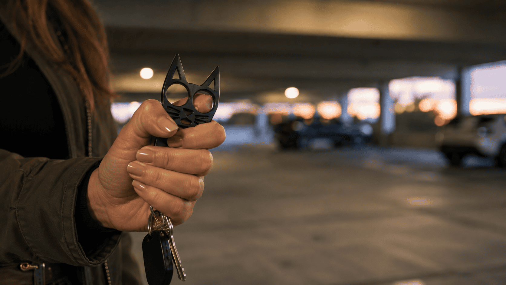 ChatGPT Image One Jun 19 2026 | Nittany Self Defense | Nittany Self Defense Close up editorial photograph of a womans hand holding a black cat ear self defense keychain in a secure grip with keys hanging below The background shows a softly blurred parking garage illuminated by warm evening light conveying confidence situational awareness and everyday personal preparedness