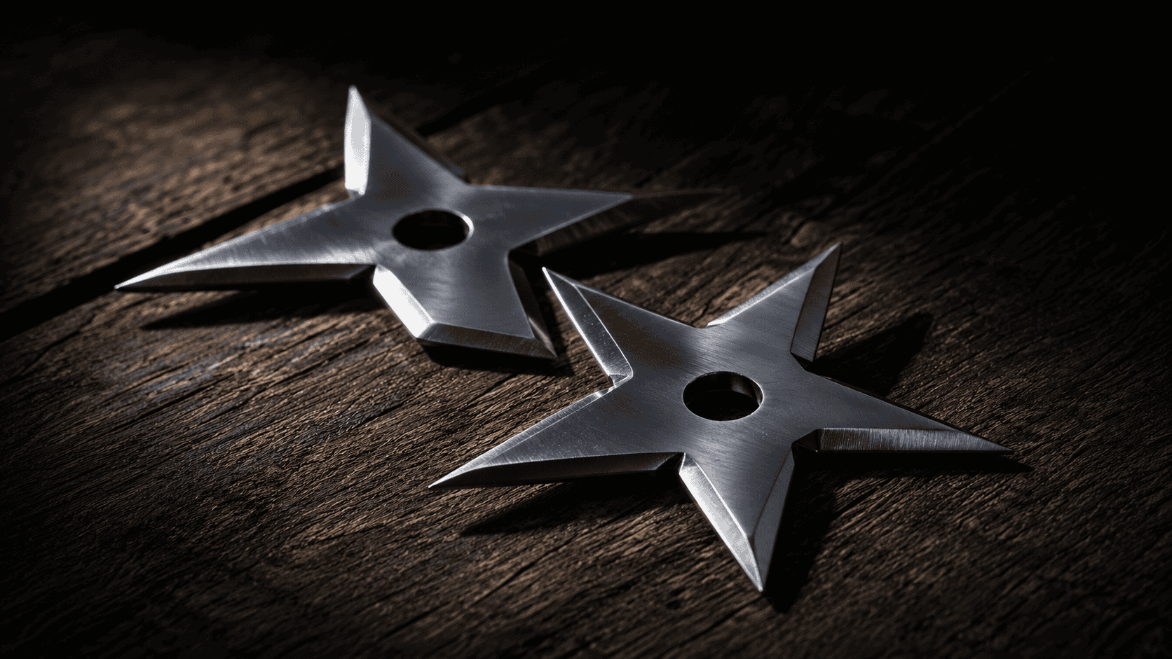Two polished stainless steel throwing stars resting on a dark weathered wooden surface